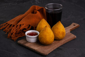 Traditional fried coxinha stuffed with chicken and a glass of cold soda.